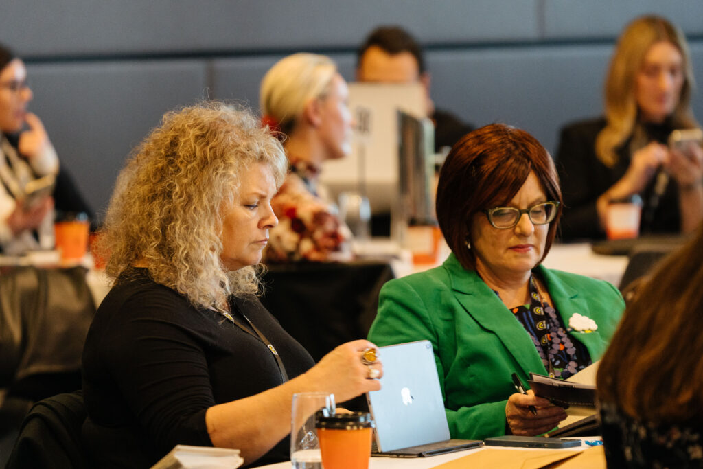 Two delegates working at a table, one on a laptop, State of Social ’21