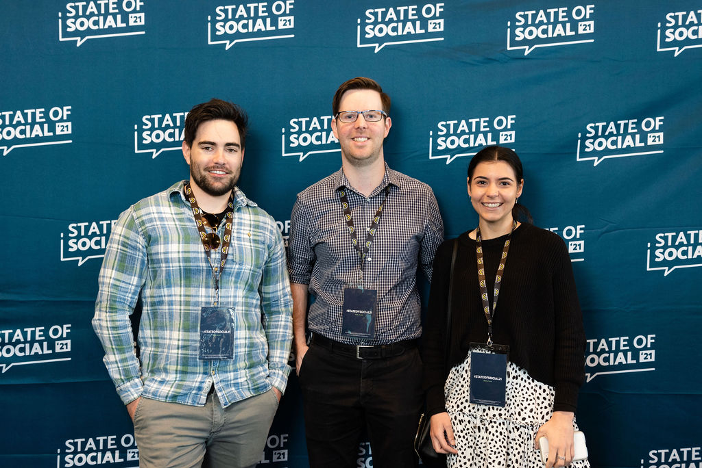 Three delegates with lanyards pose in front of the State of Social backdrop, State of Social ’21