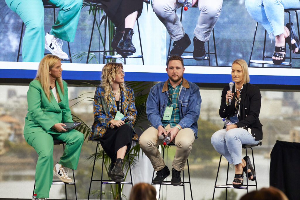 Four panellists seated on stools on stage with the audience's screen behind them, State of Social ’23