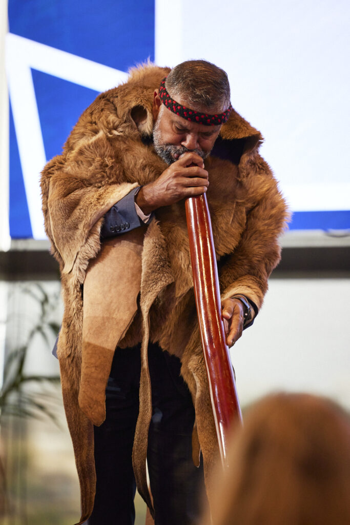 Man in a fur cloak holds a decorated staff on stage, State of Social ’23
