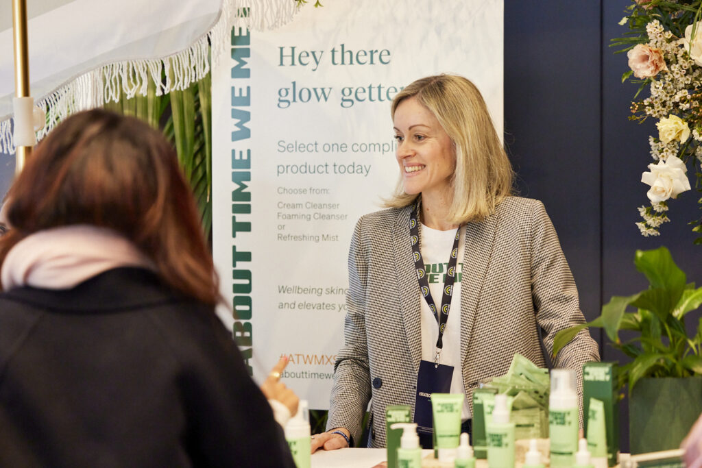 Woman at a partner stand surrounded by skincare products and flowers, State of Social ’23