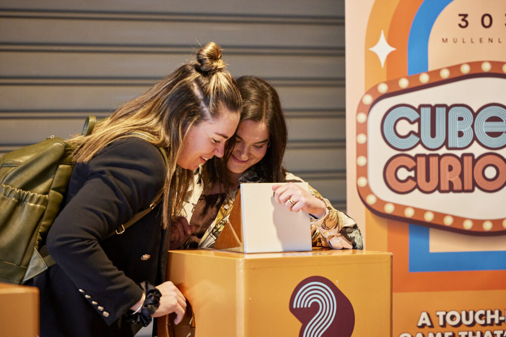 Two delegates peer into a Cube Curious game box, State of Social ’23