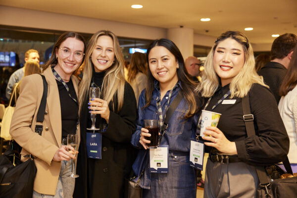 Four delegates with drinks and lanyards smile for the camera, State of Social ’23