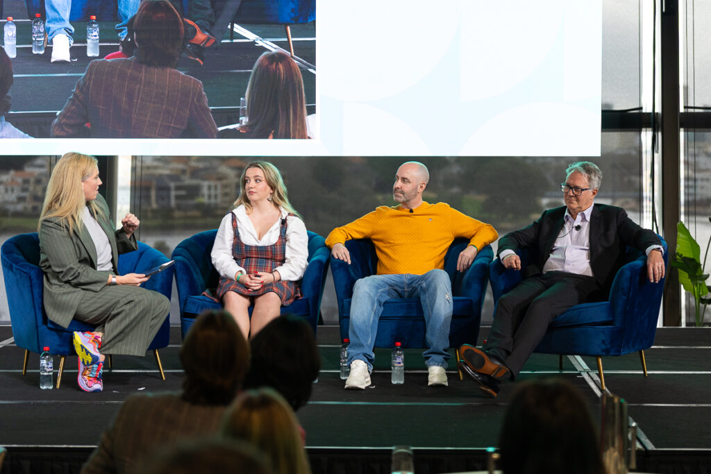 Four panellists on stage with armchairs and a facilitator