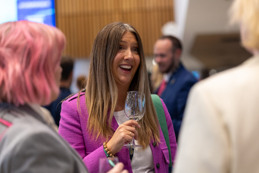 Delegate in a pink blazer laughs and holds a glass, State of Social ’25
