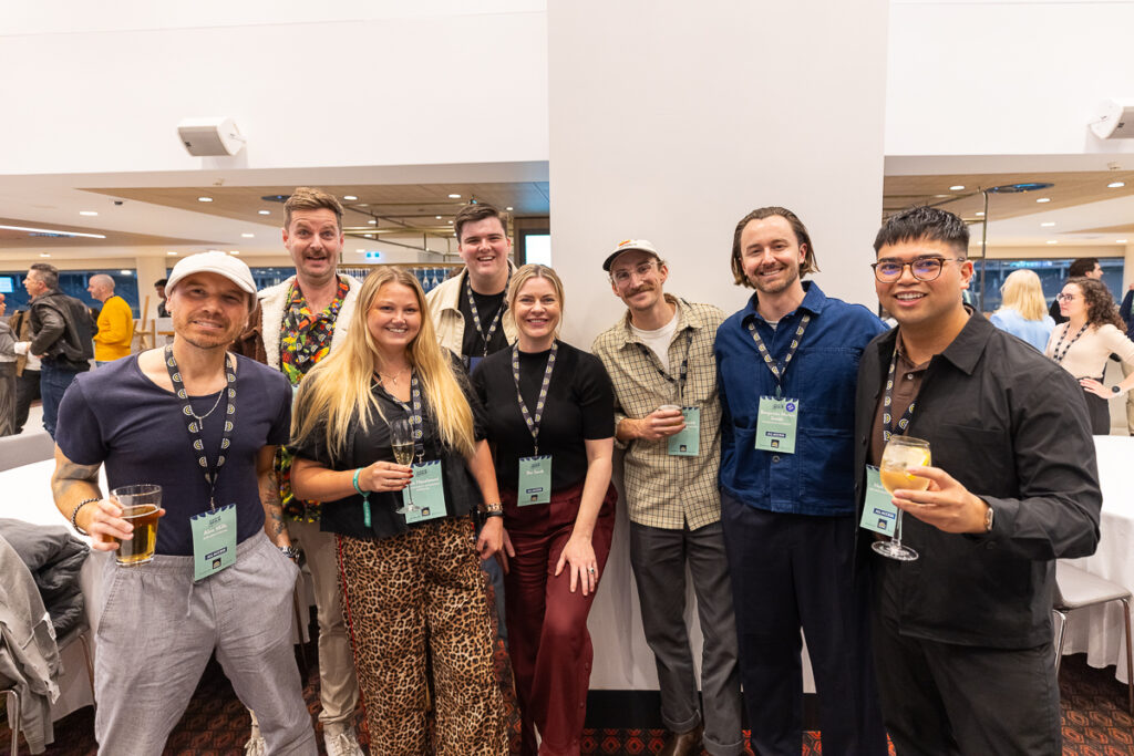 Seven delegates hold drinks and pose together at the networking drinks, State of Social ’25