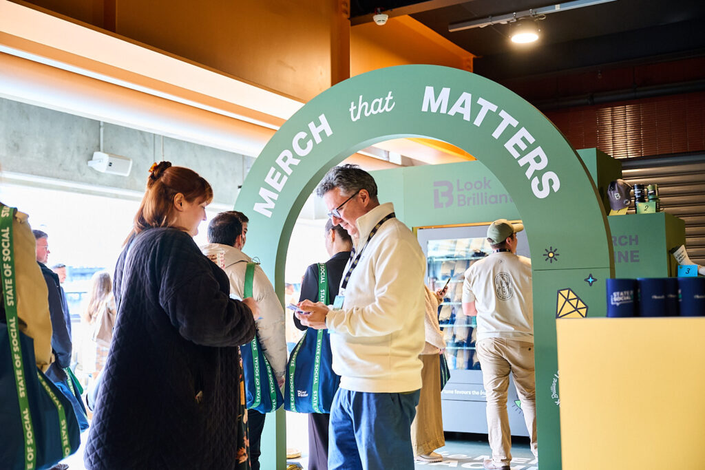 Delegates browse the green arched Merch that Matters stand, State of Social ’25