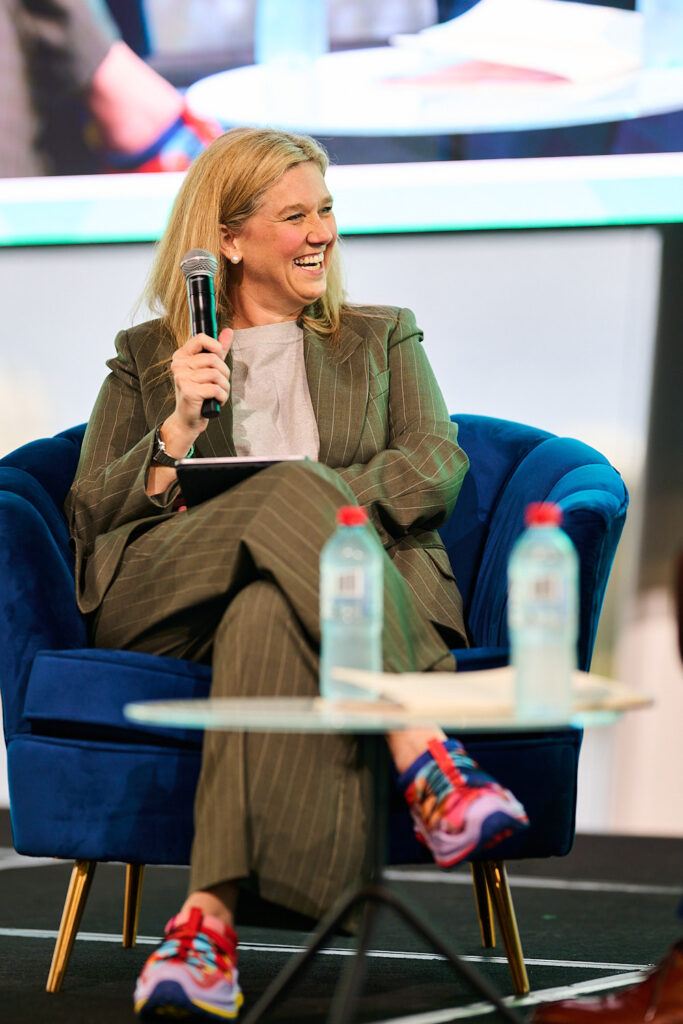 Speaker in an olive suit and bright trainers holds a microphone on stage, State of Social ’25