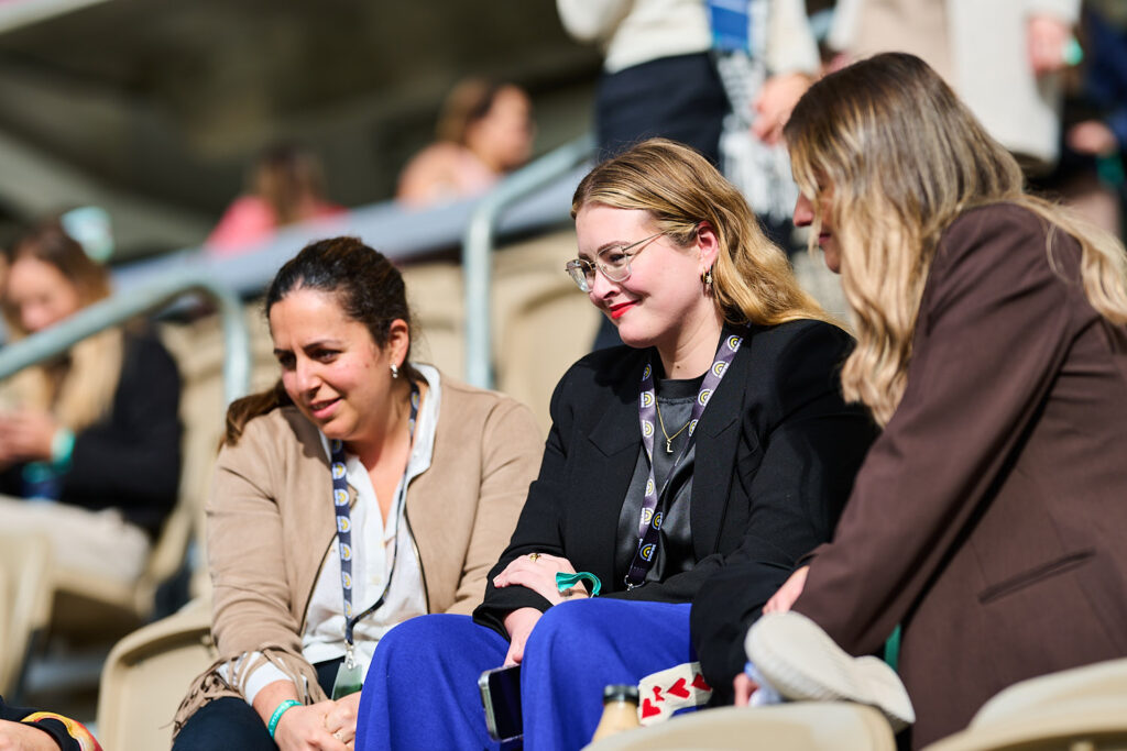 Three delegates laugh together in the stadium seating, State of Social ’25