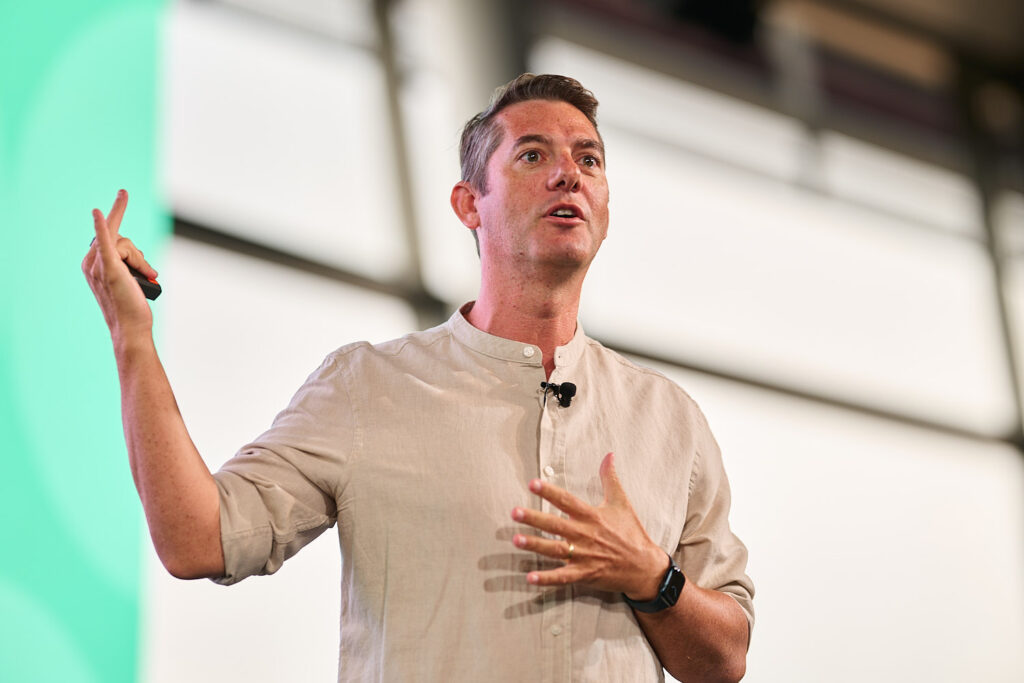 Speaker in a linen shirt gestures as he presents in front of a green screen