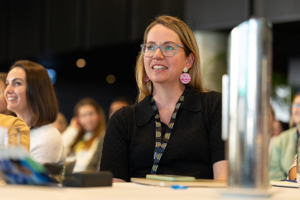 Delegate in glasses and a lanyard smiles at a table