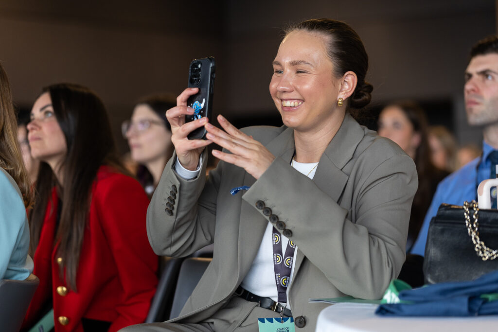 Delegate in a grey blazer laughs while filming on her phone