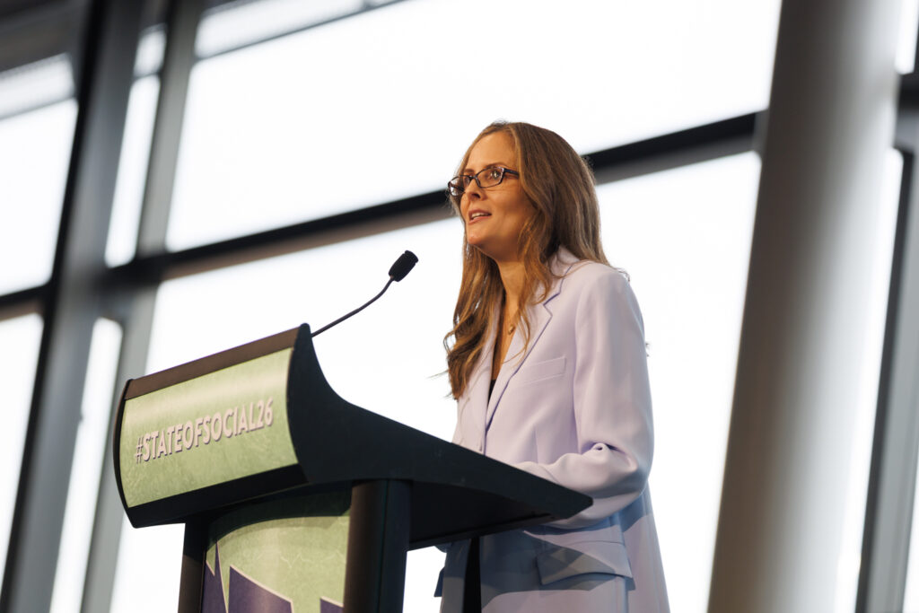 Speaker in a pale suit presents at the State of Social lectern, State of Social ’26