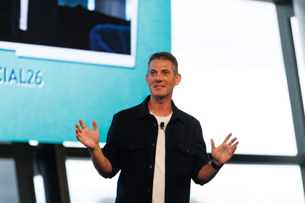 Speaker in a black shirt opens his arms in front of a screen, State of Social ’26