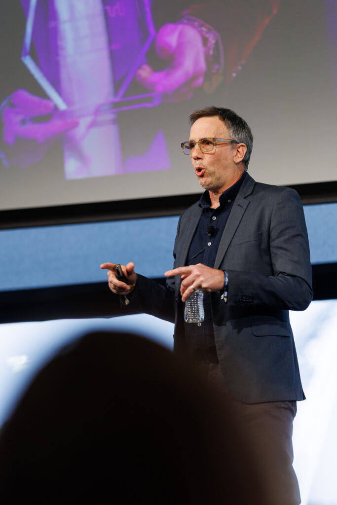 Speaker in a charcoal blazer presents in front of a purple screen, State of Social ’26