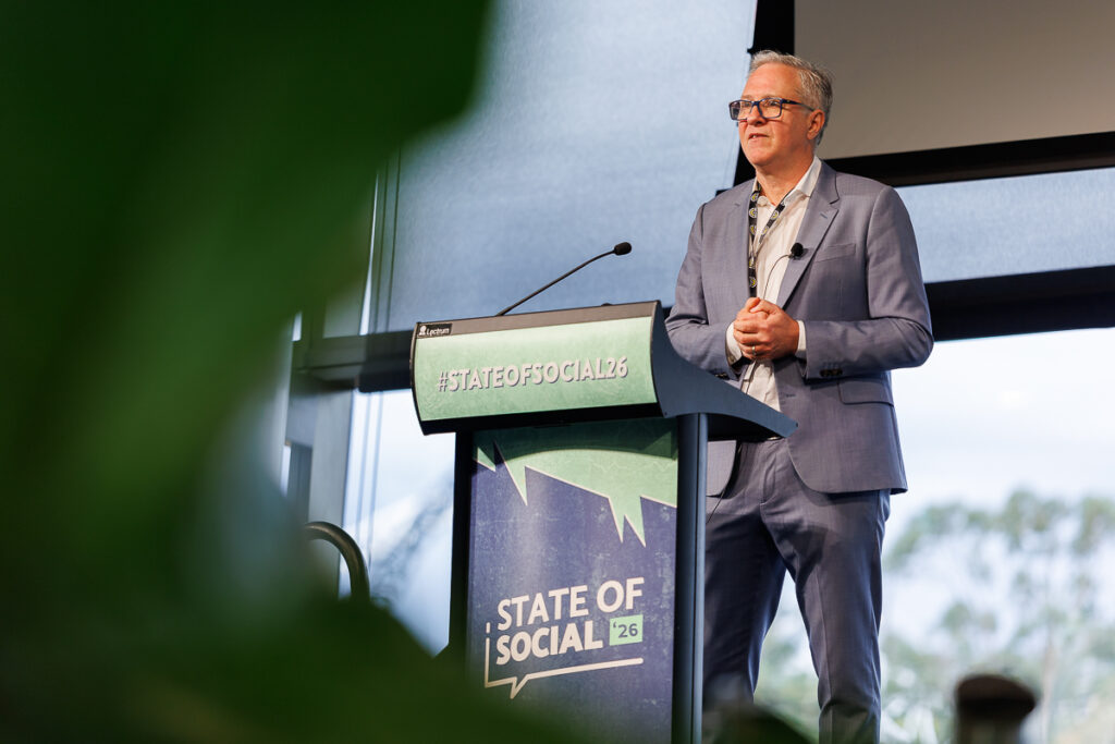 Speaker in a grey blazer presents at the State of Social lectern, State of Social ’26