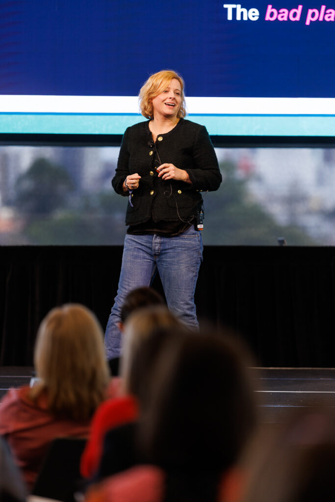 Speaker in black stands on stage in front of a large screen, State of Social ’26