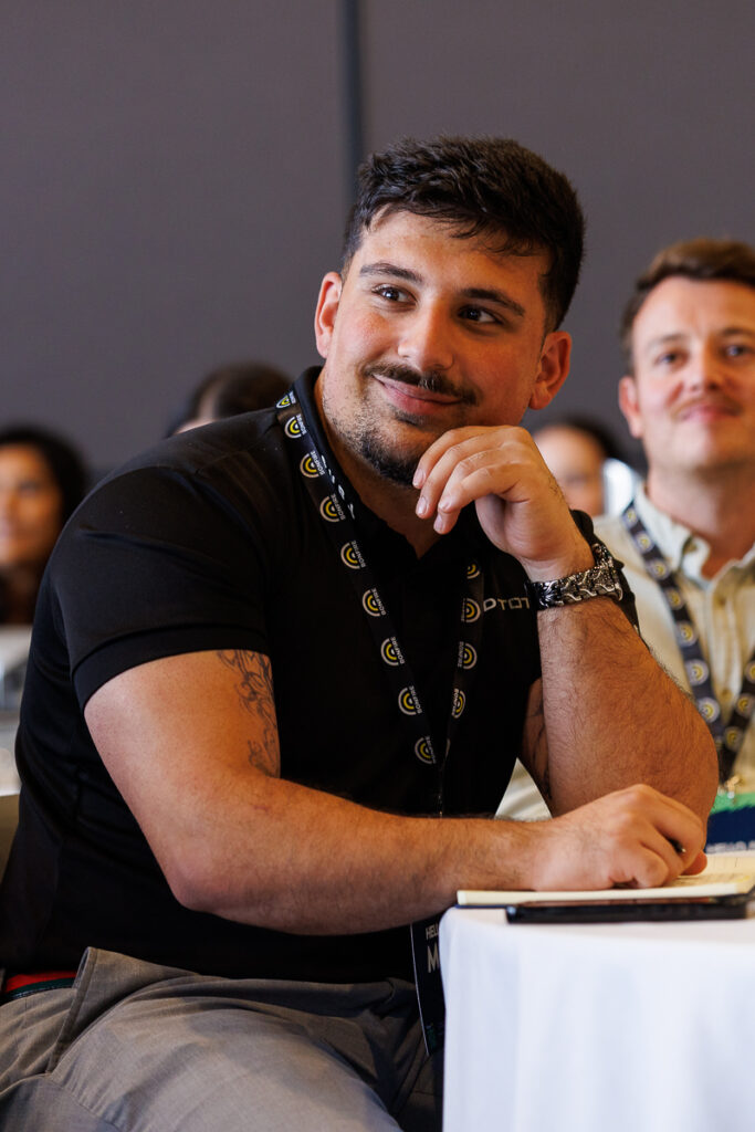Delegate in a black t-shirt sits at a table with a lanyard, State of Social ’26