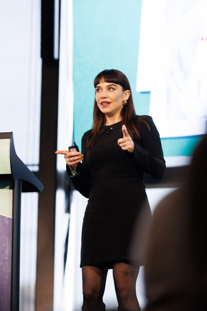 Speaker in a black dress gestures on stage, State of Social ’26