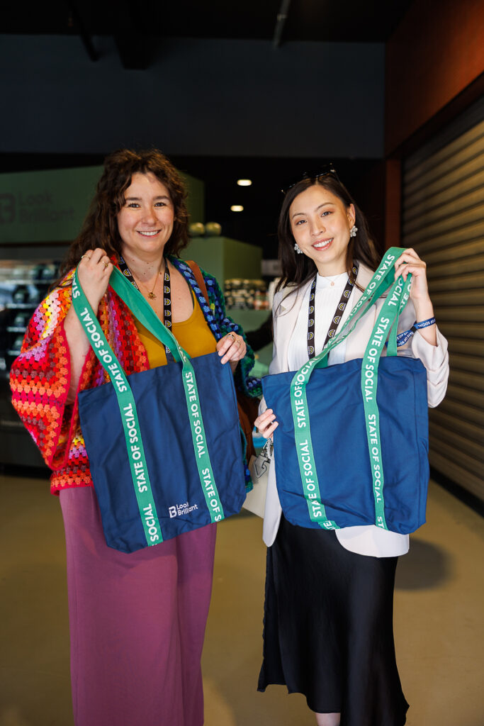 Two delegates hold up colourful woven tote bags, State of Social ’26